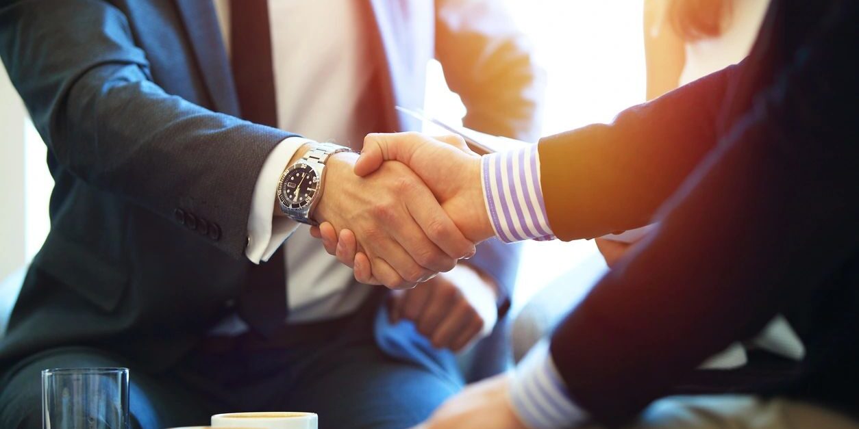 Two people shaking hands over a table.